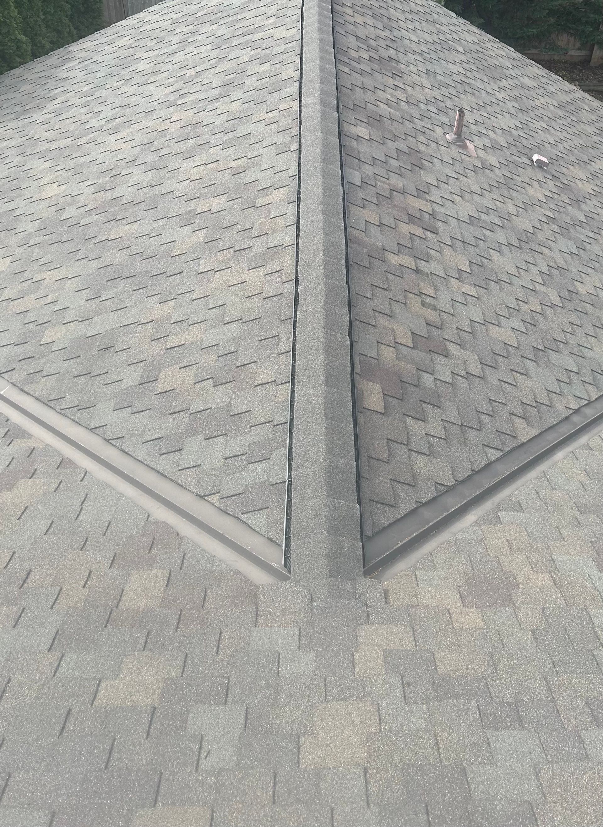A high-angle view of a gray asphalt shingle roof featuring a central ridge, hip rafters, and metal flashing.