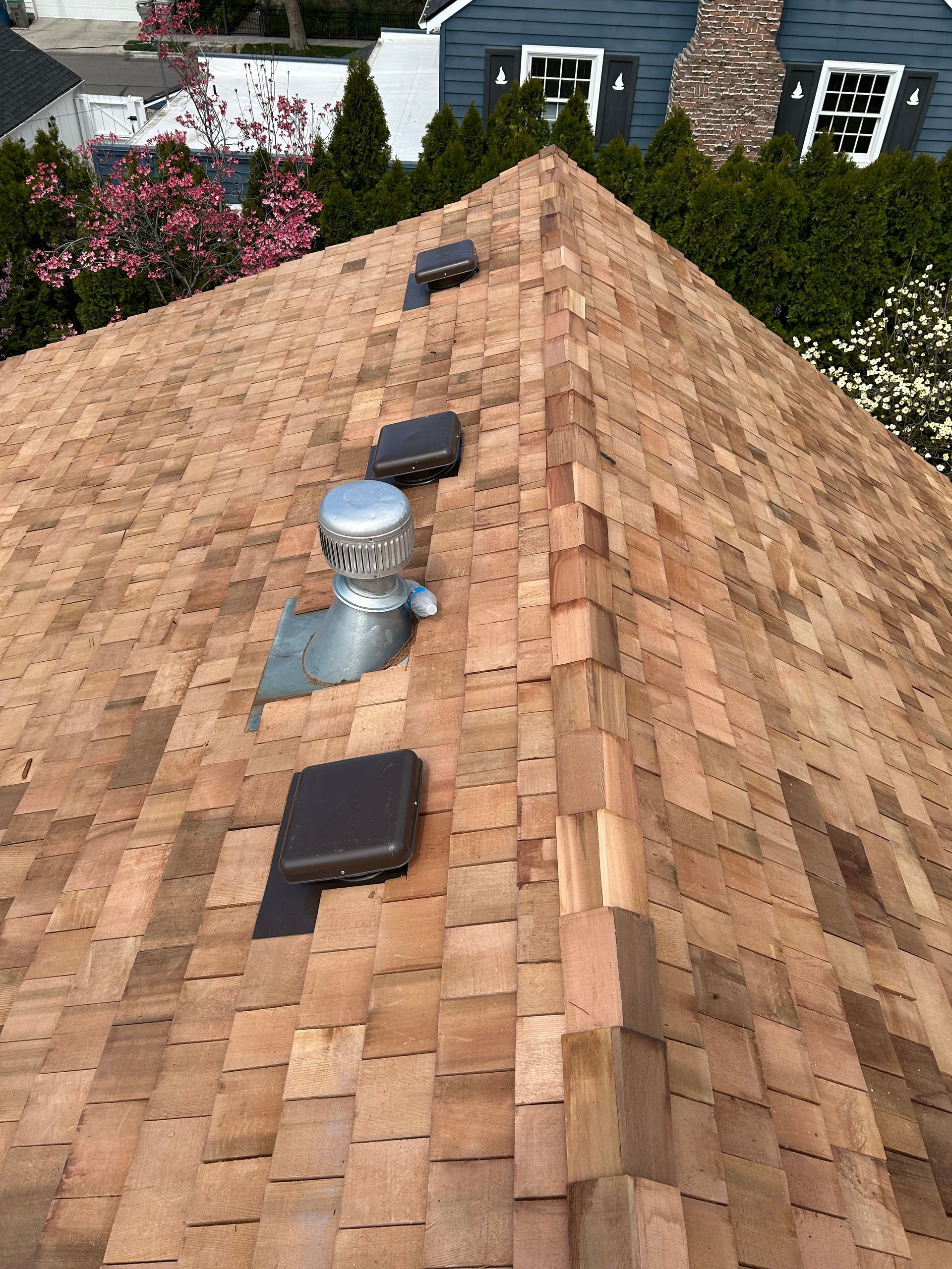 Brown shingled roof with a silver metal chimney vent and three dark box vents along the ridge line.