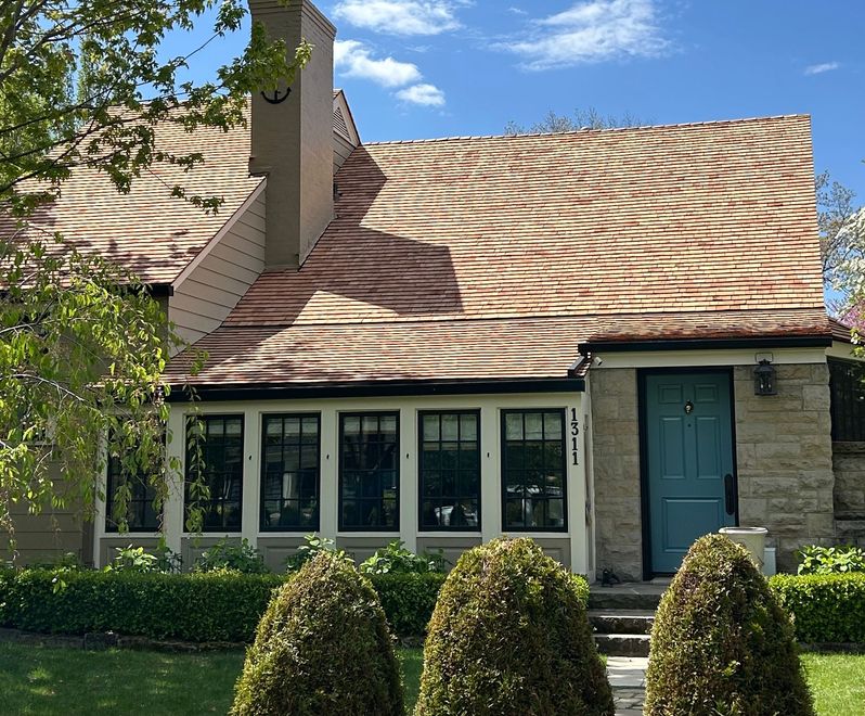 House with textured brown and tan roof, teal door, stone facade, and manicured landscaping.