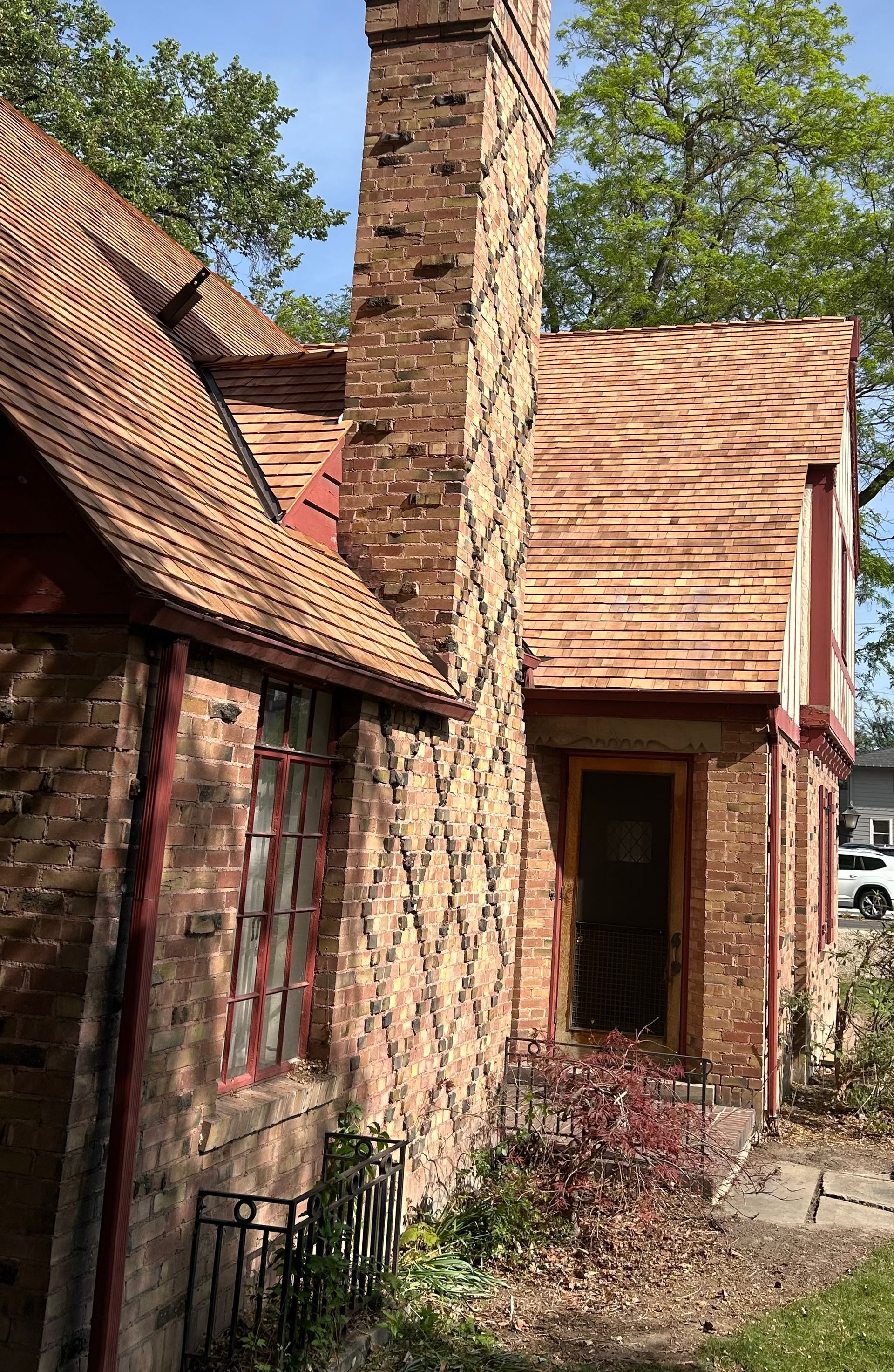 A Tudor-style home with a brick chimney featuring a decorative diamond pattern, a multi-gabled roof, and a front entry.