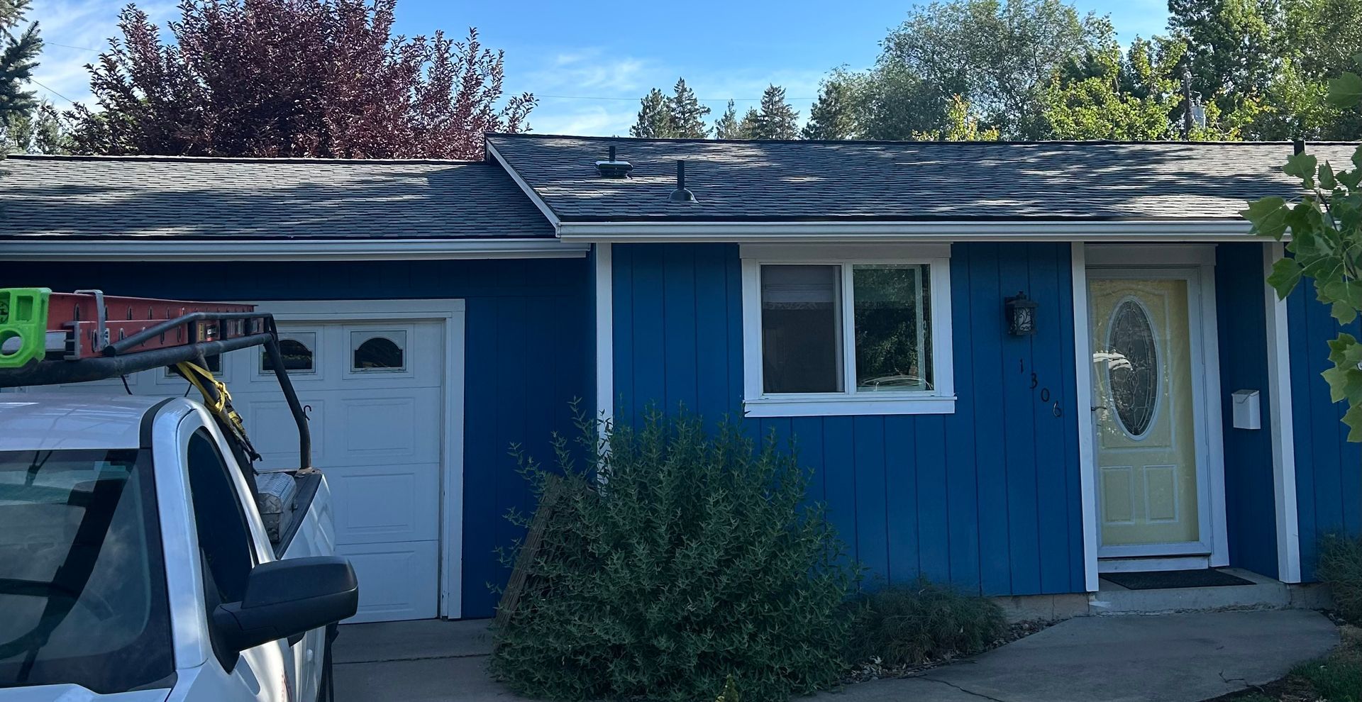 A blue house with a white front door and window, featuring a worn roof and a work truck parked in front.
