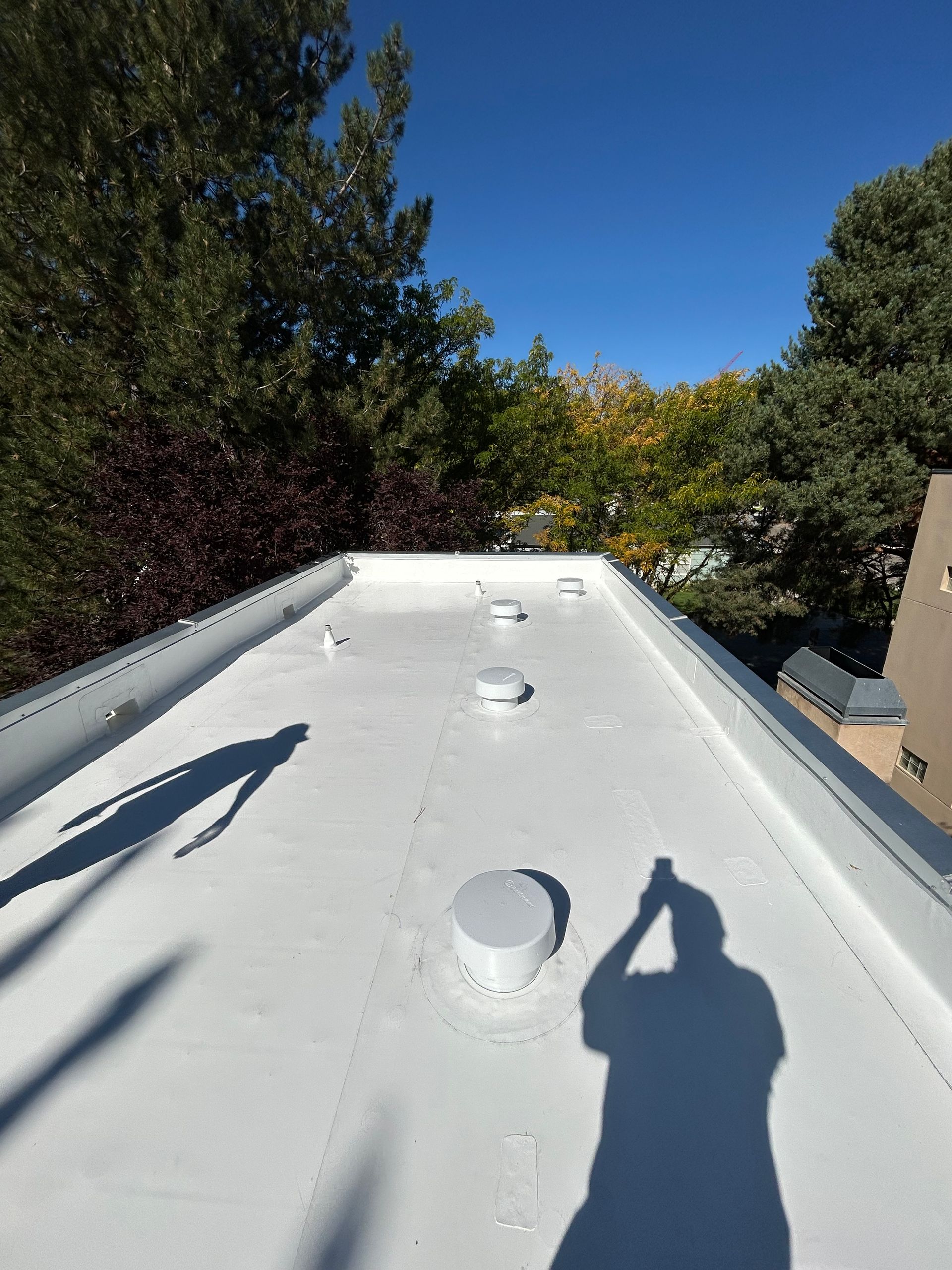 A white flat roof with several vents, seen from above, with shadows of two people visible on the surface.