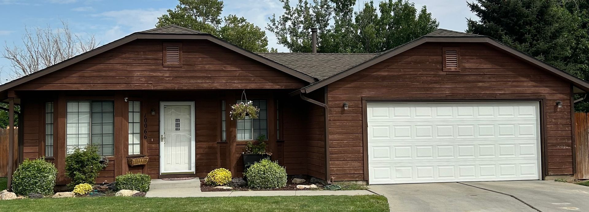 A single-story house with dark brown wood siding, a white front door, and a two-car white garage door.