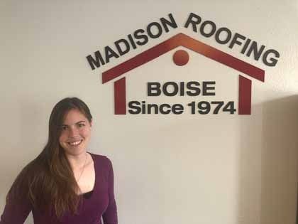 Woman smiling, standing next to a Madison Roofing logo on a wall, Boise, established in 1974.