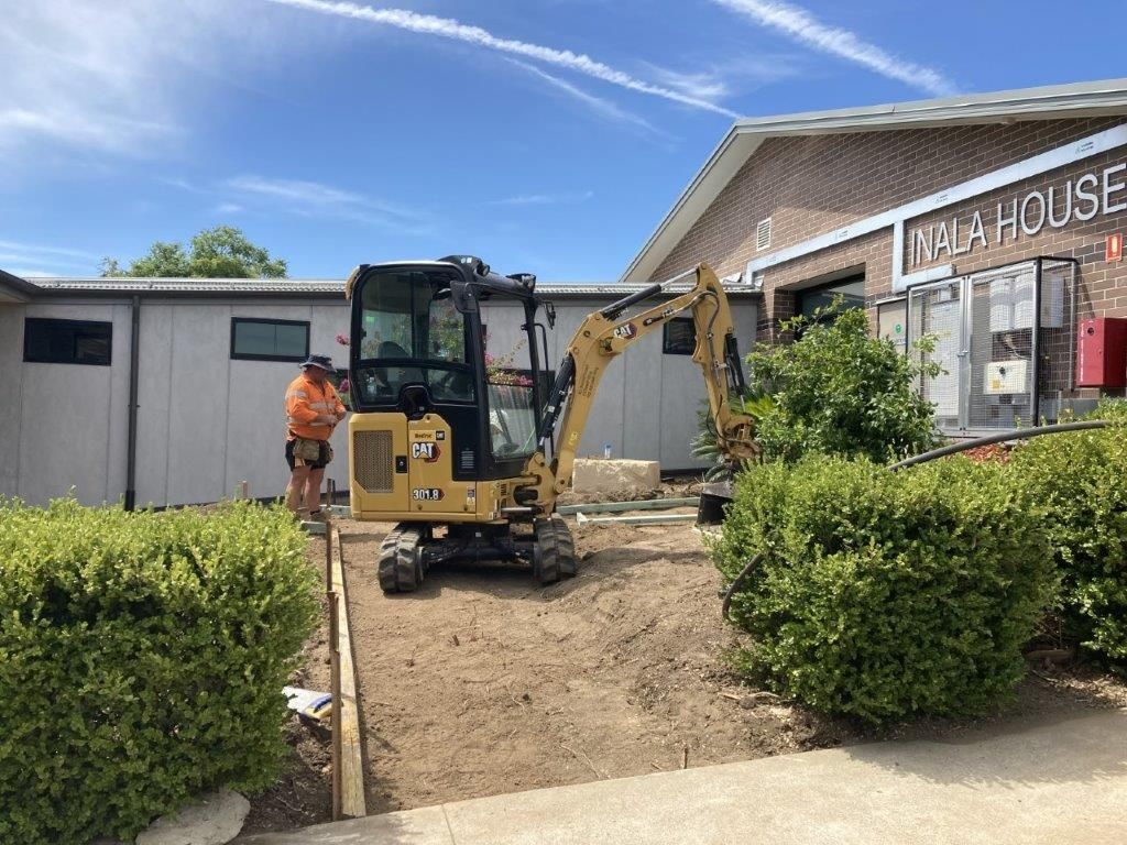 Yellow excavator digging near a building with a worker present.
