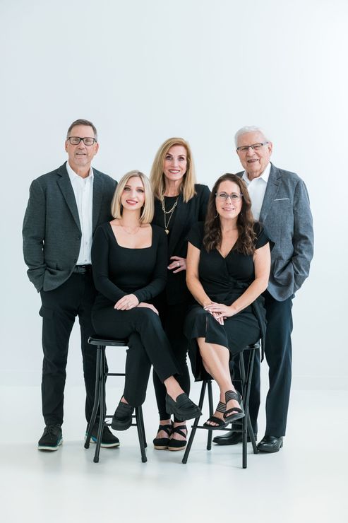 Five coworkers posing in a bright studio, two seated in front and three standing behind.