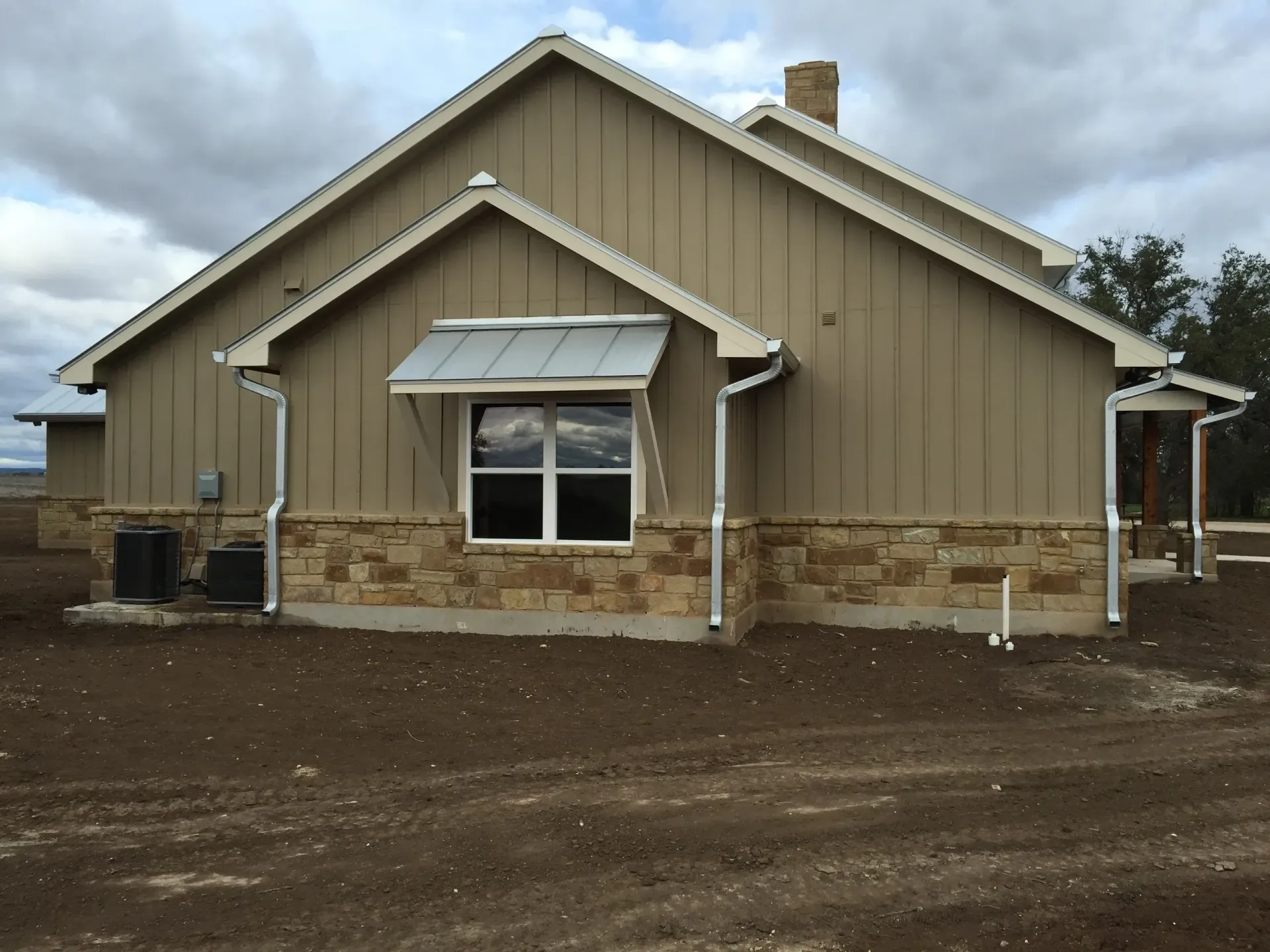 Tan house with stone base, white window trim, and a metal awning.