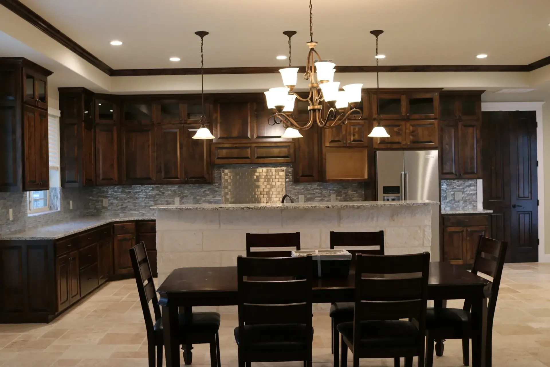 Dark wood kitchen with dining table and chandelier.