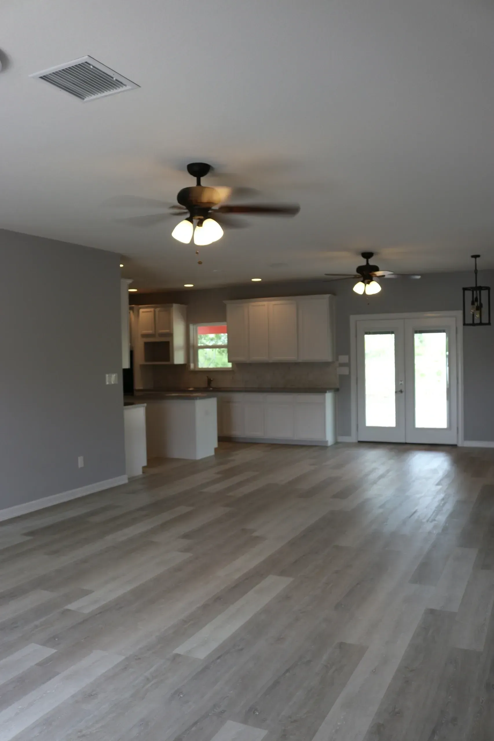 An empty, open-concept living space with gray walls and wood-look flooring. A kitchen is in the background.