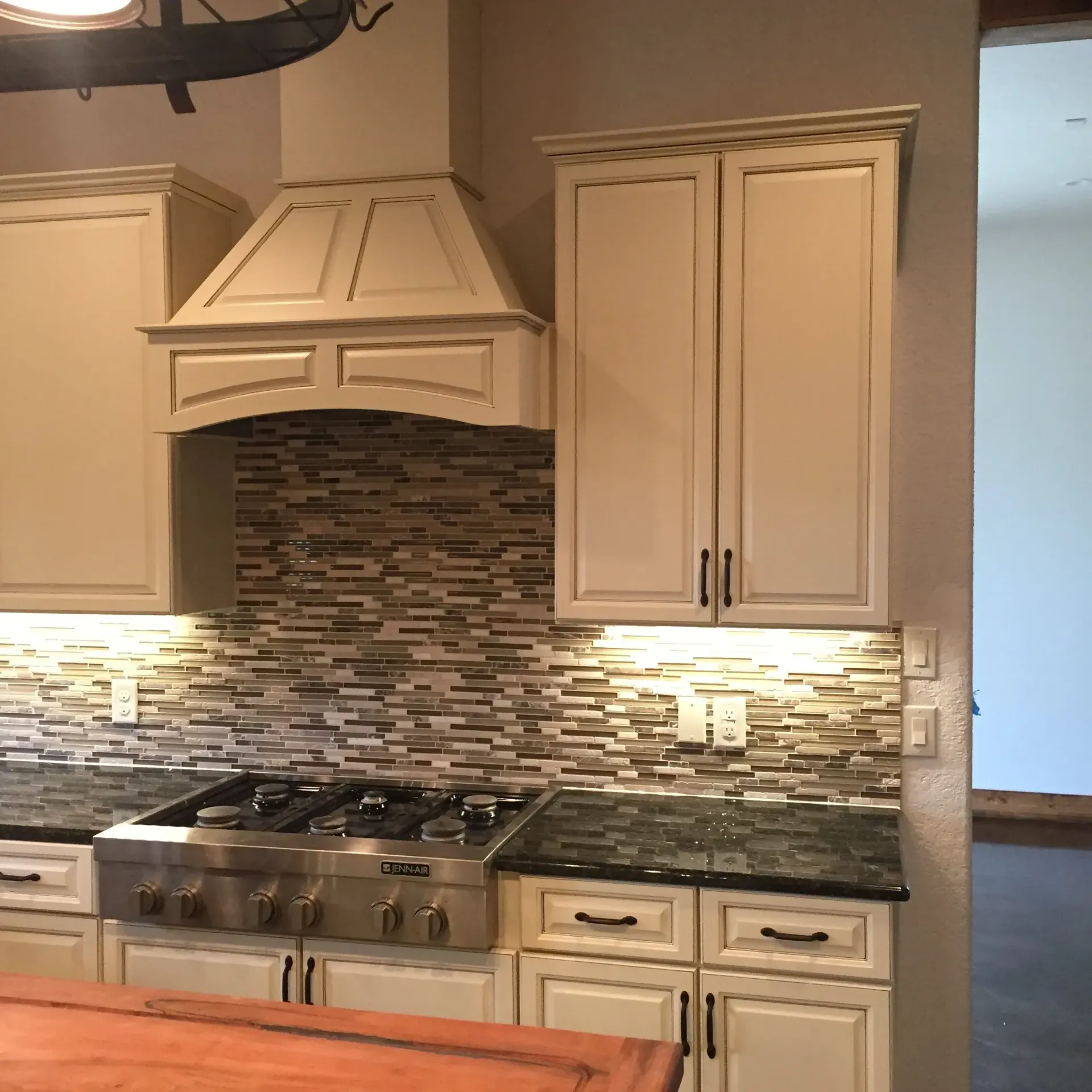 Kitchen with white cabinets, stone backsplash, range, and hood.