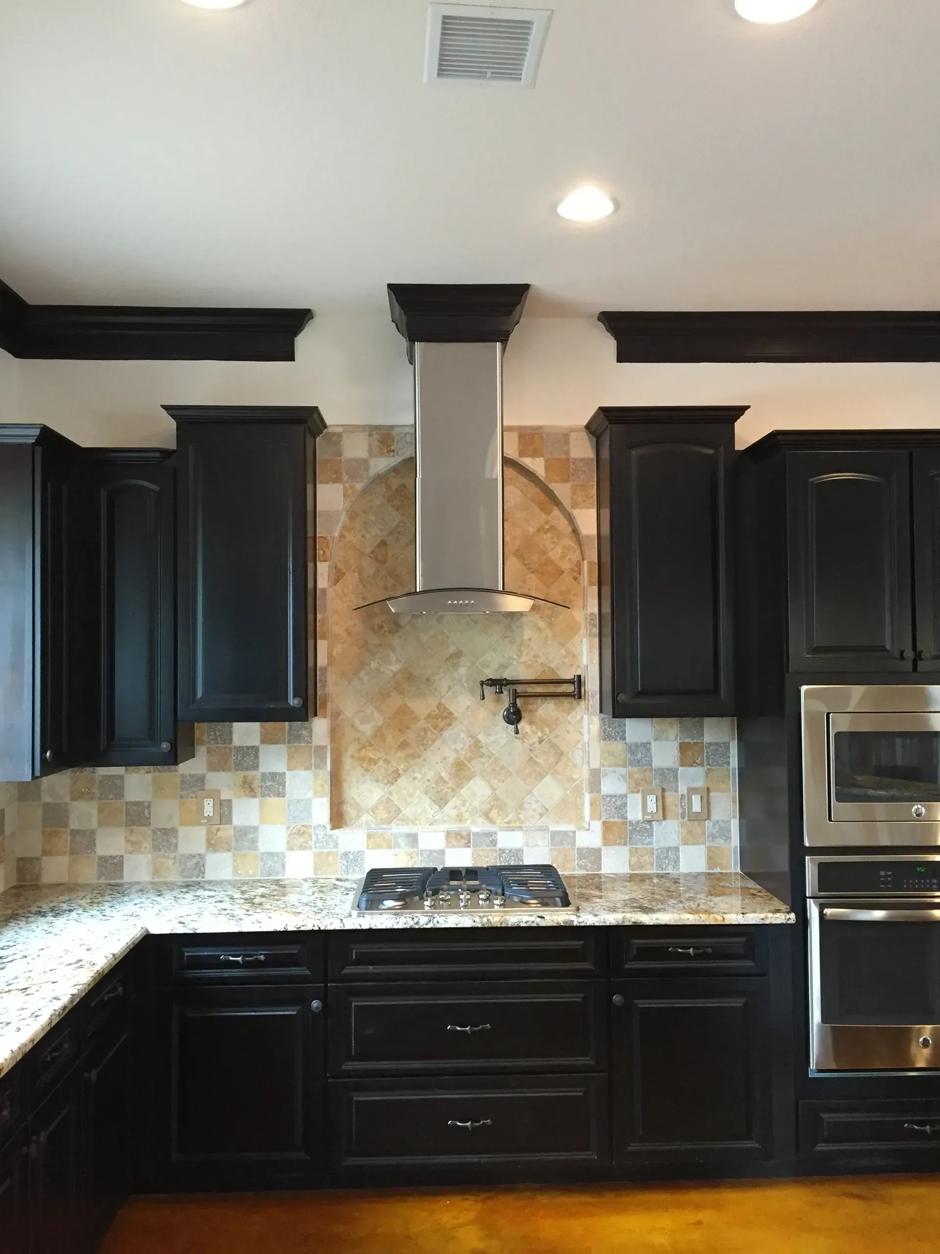 Black kitchen cabinets with stainless steel range hood, granite countertops, and patterned backsplash.