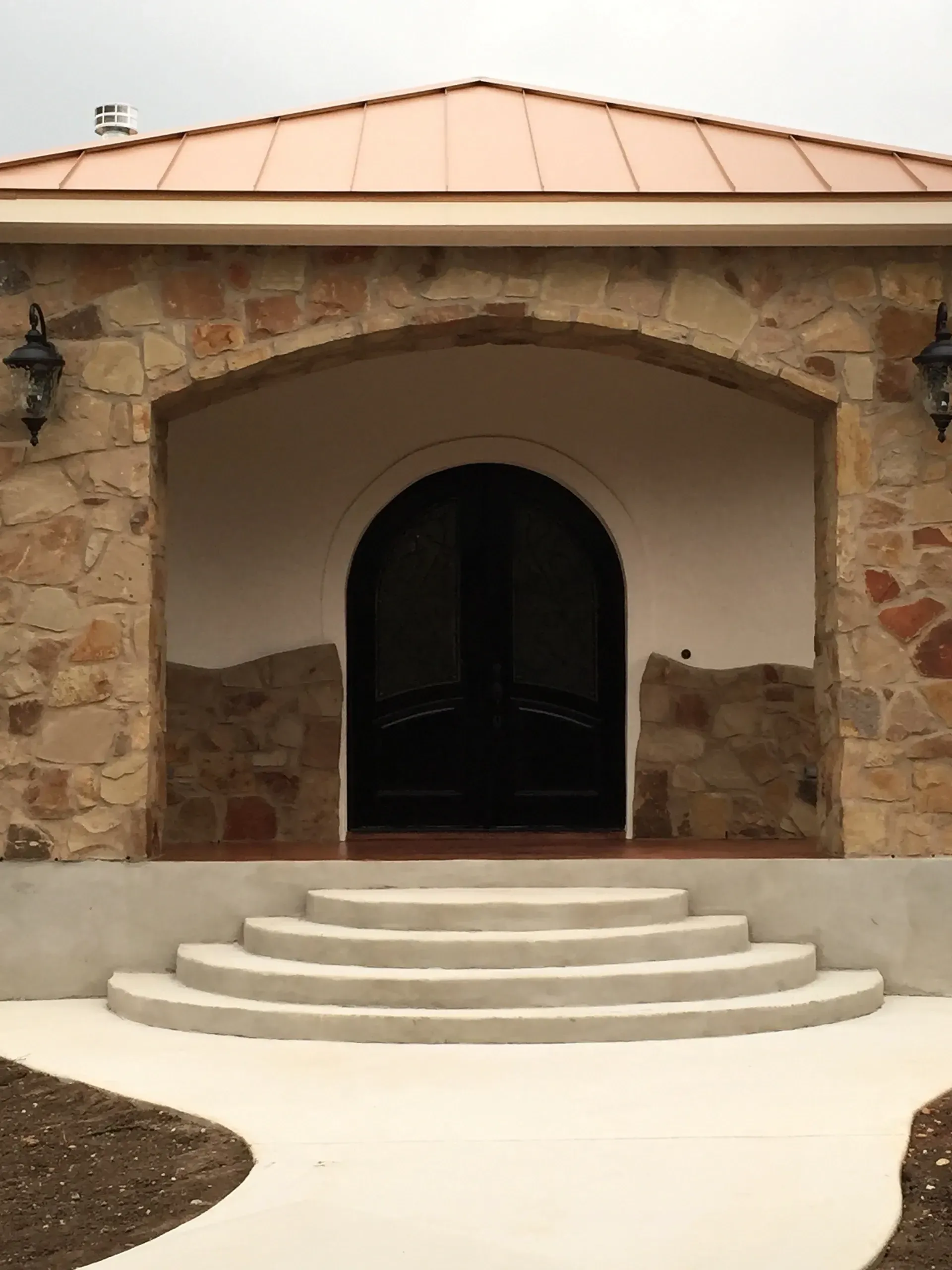 Stone facade building with arched doorway, steps, and copper roof.