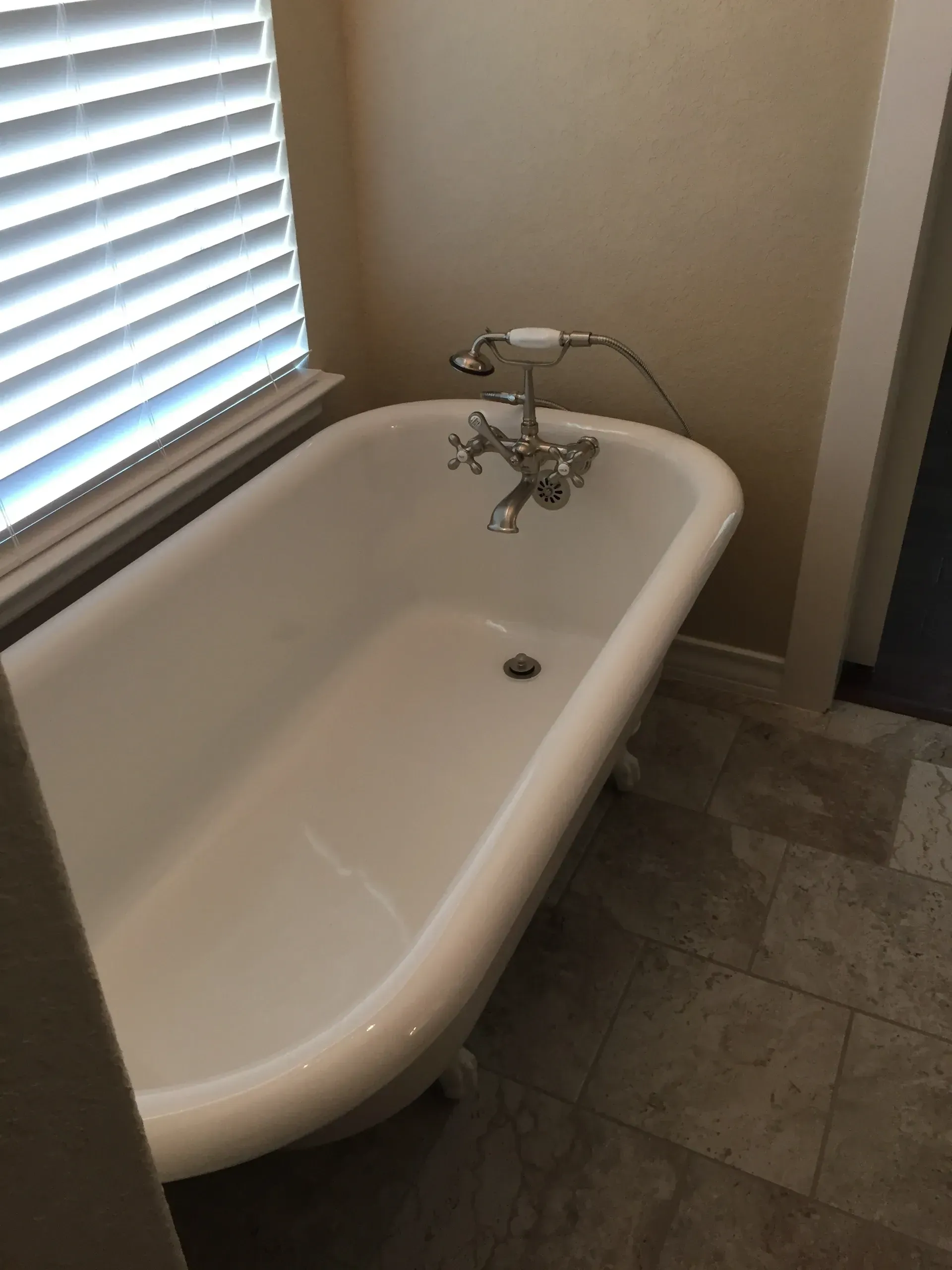 Clawfoot bathtub in a bathroom, with a window and tile flooring.