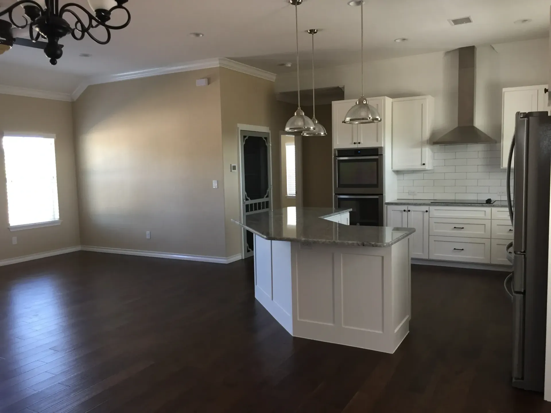 Open-concept kitchen and living area with hardwood floors, white cabinets, and a gray granite island.