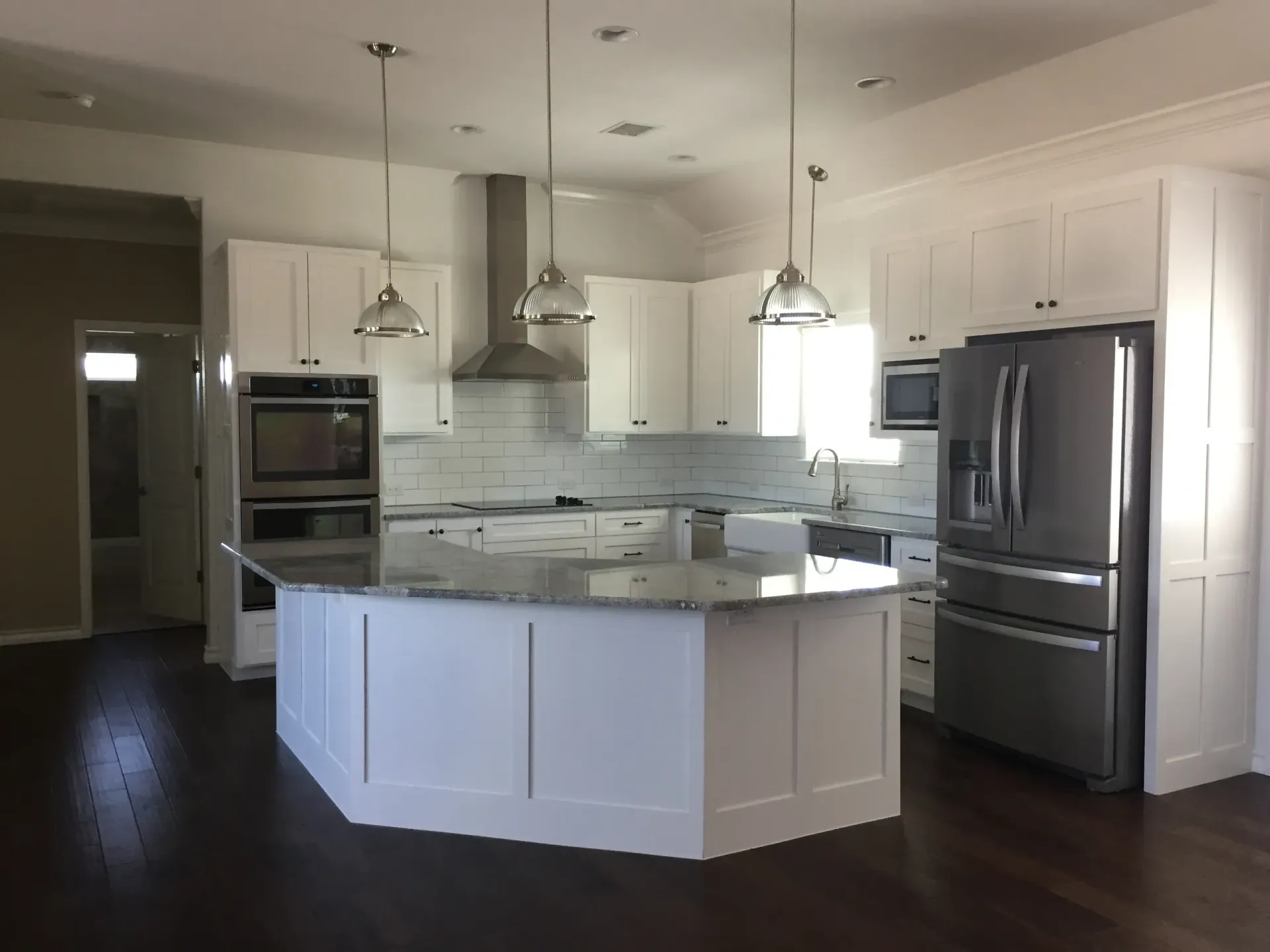 White kitchen with island, stainless steel appliances, dark wood floors, and pendant lights.