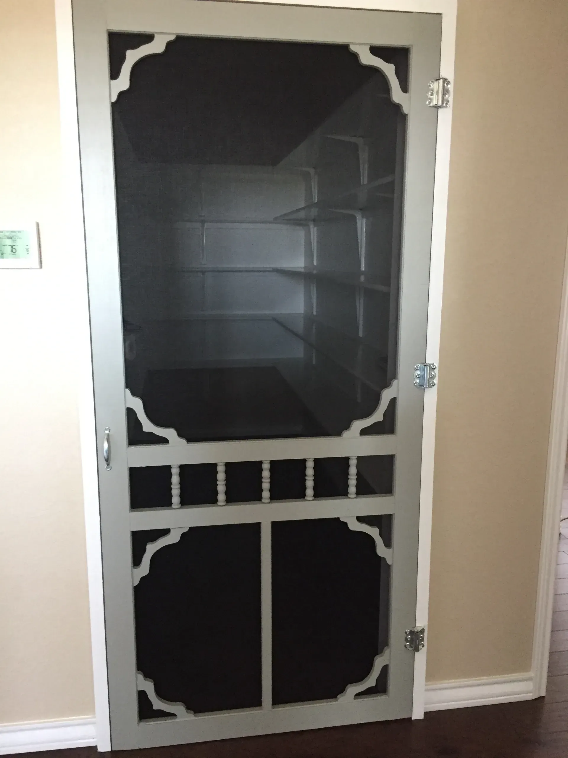 Gray screen door with decorative cutouts, set in a light-colored doorway.