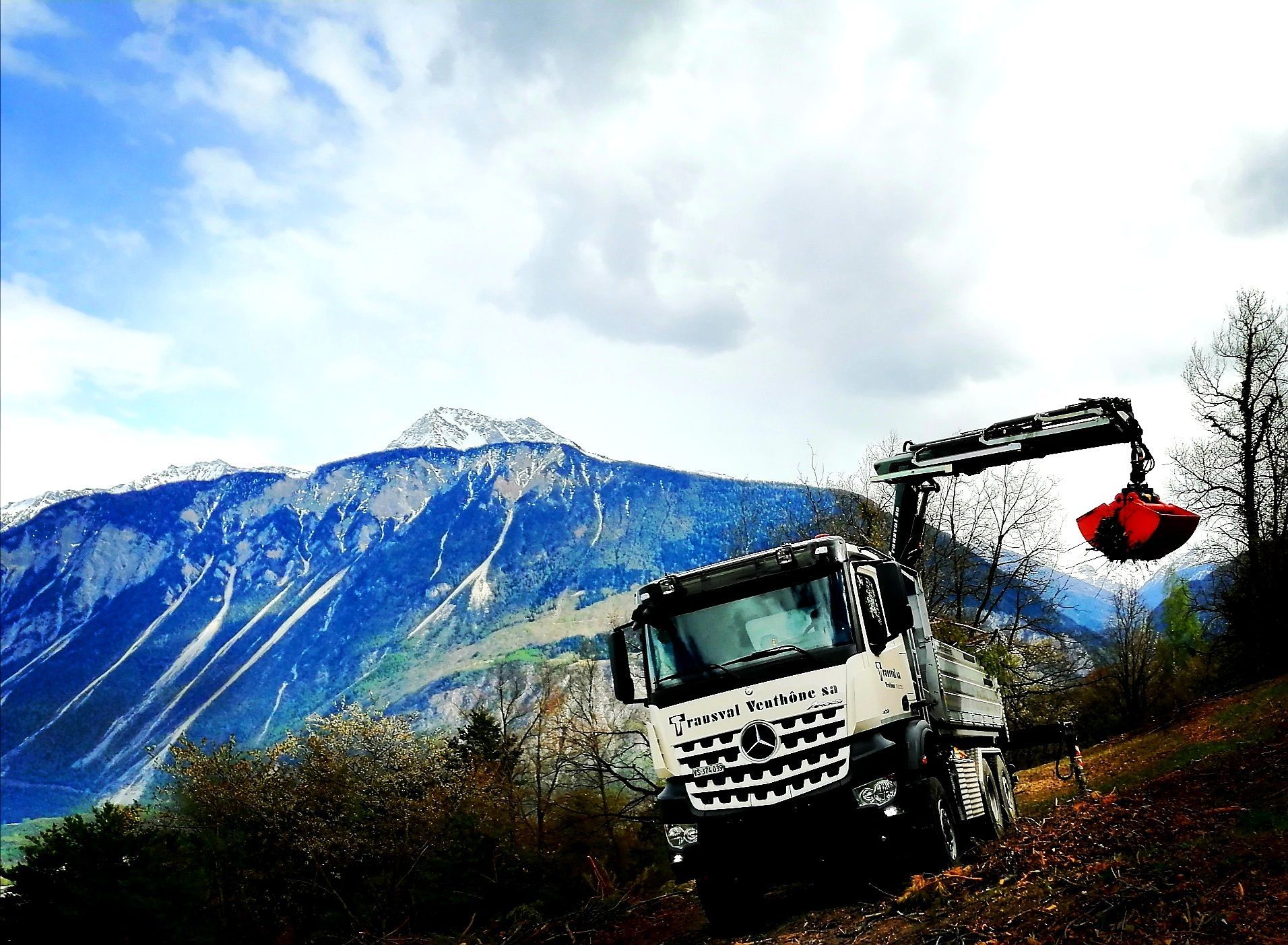 Un camion avec une grue attachée est garé sur une colline devant une montagne.