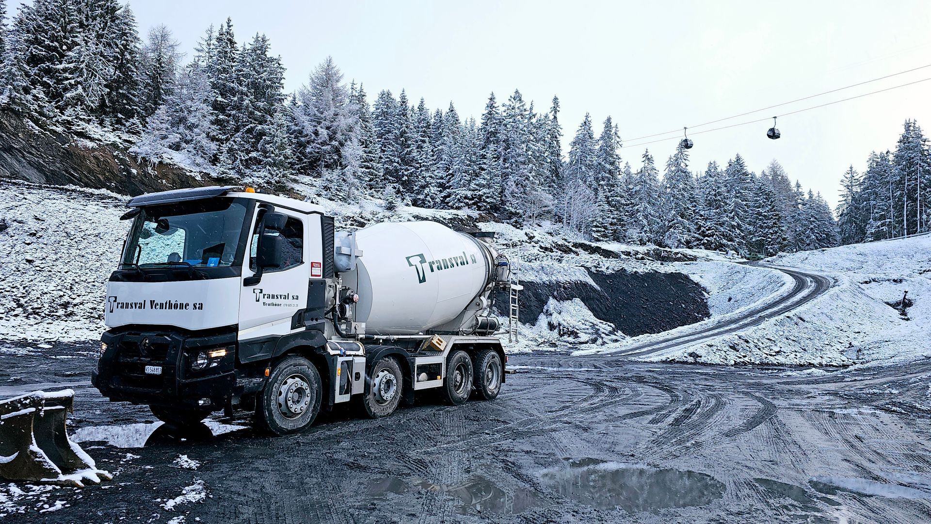 Un camion malaxeur à béton roule sur une route enneigée.