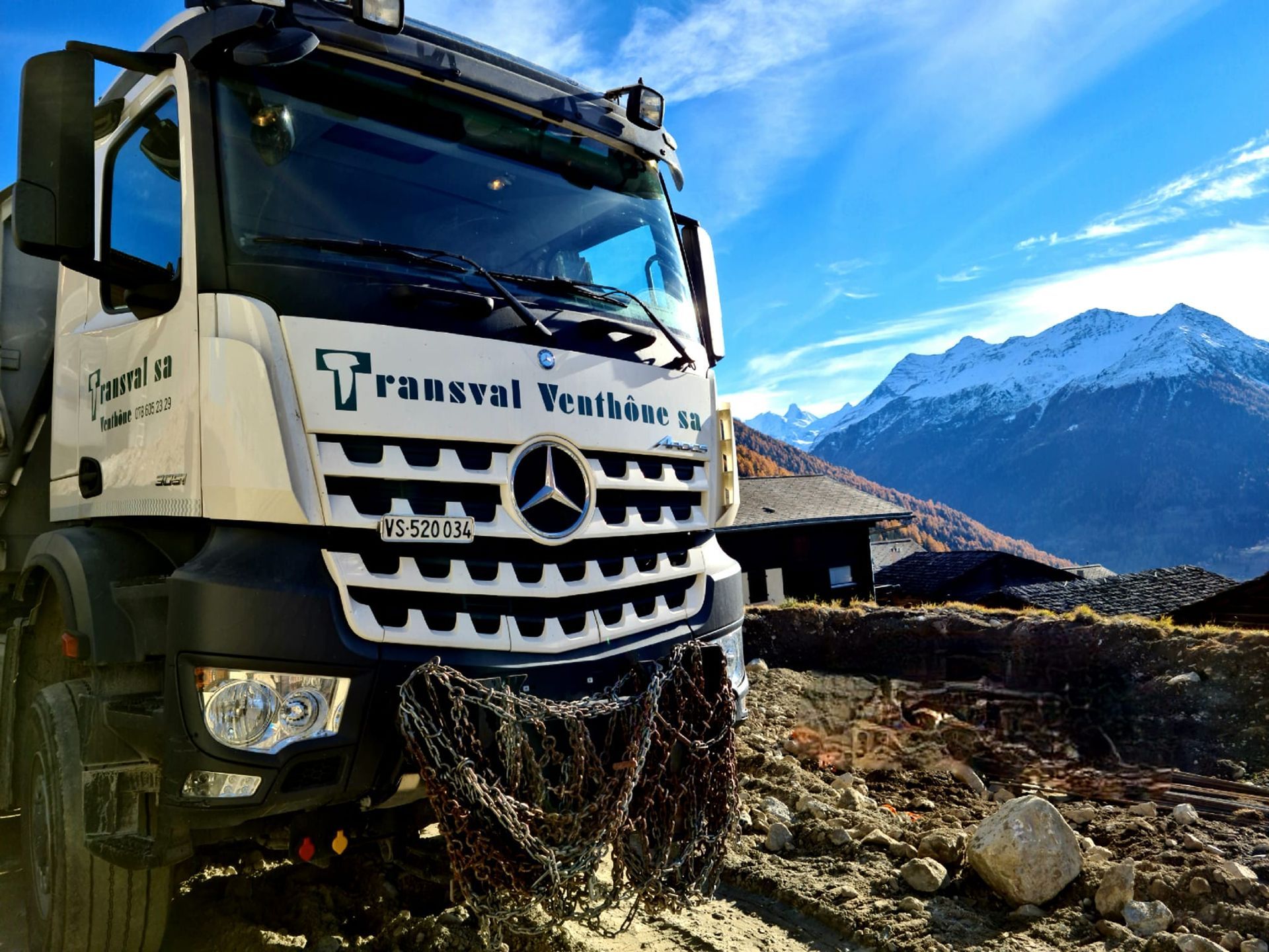 Un camion Mercedes est garé sur un chemin de terre avec des montagnes en arrière-plan.