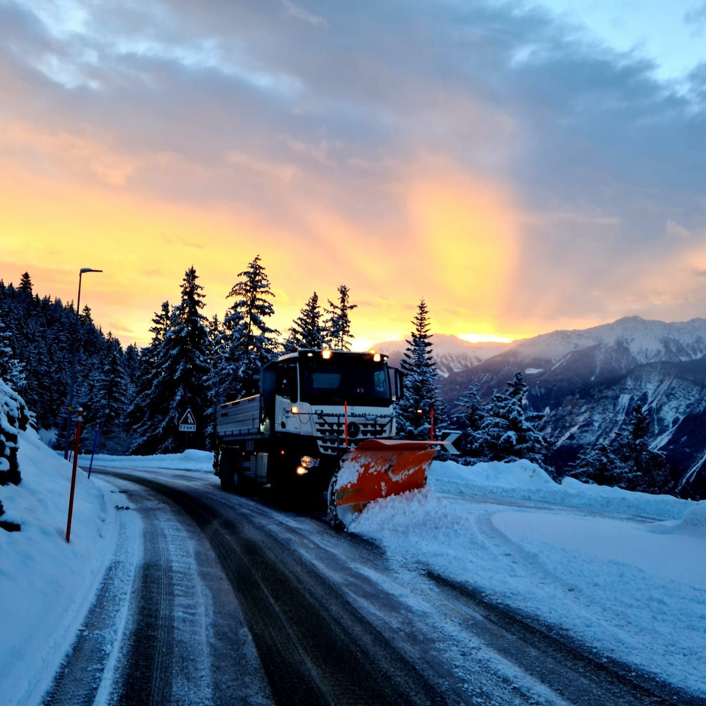 Un chasse-neige descend une route enneigée au coucher du soleil