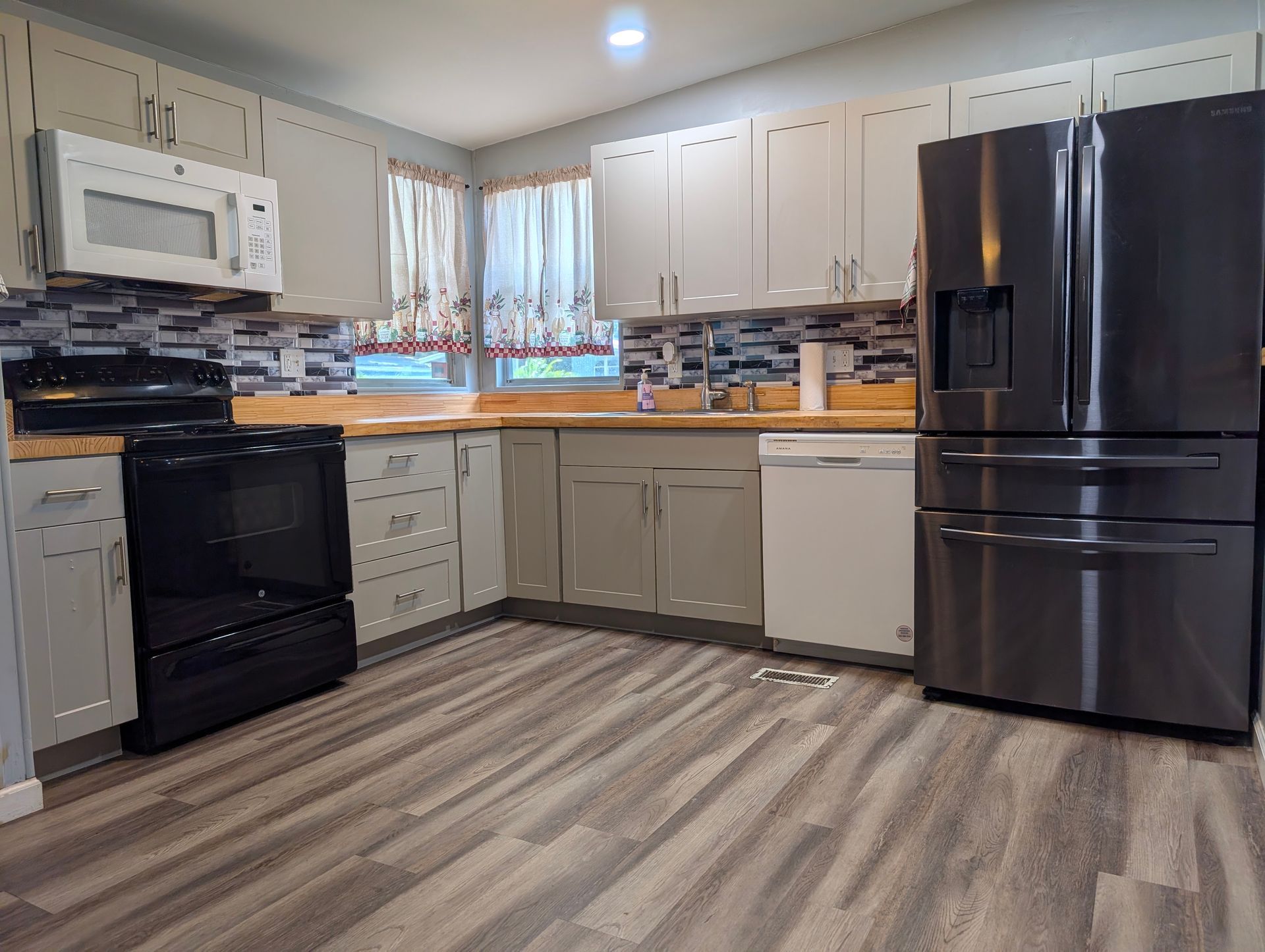 Kitchen with white cabinets, black appliances, stainless steel fridge, and wood-look flooring