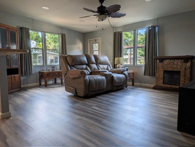 Living room with gray walls, large windows, recliner sofa, fireplace, and wood-look flooring