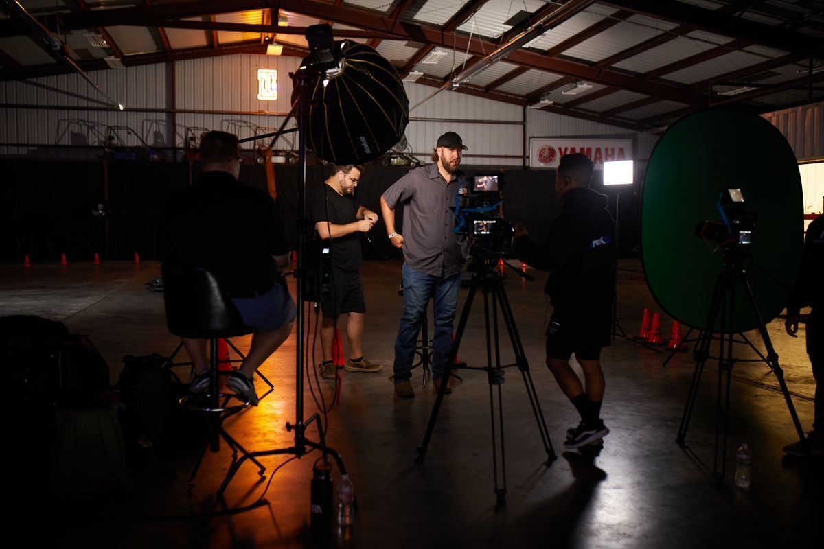 Film crew setting up lights and cameras in a dim studio with orange floor lighting