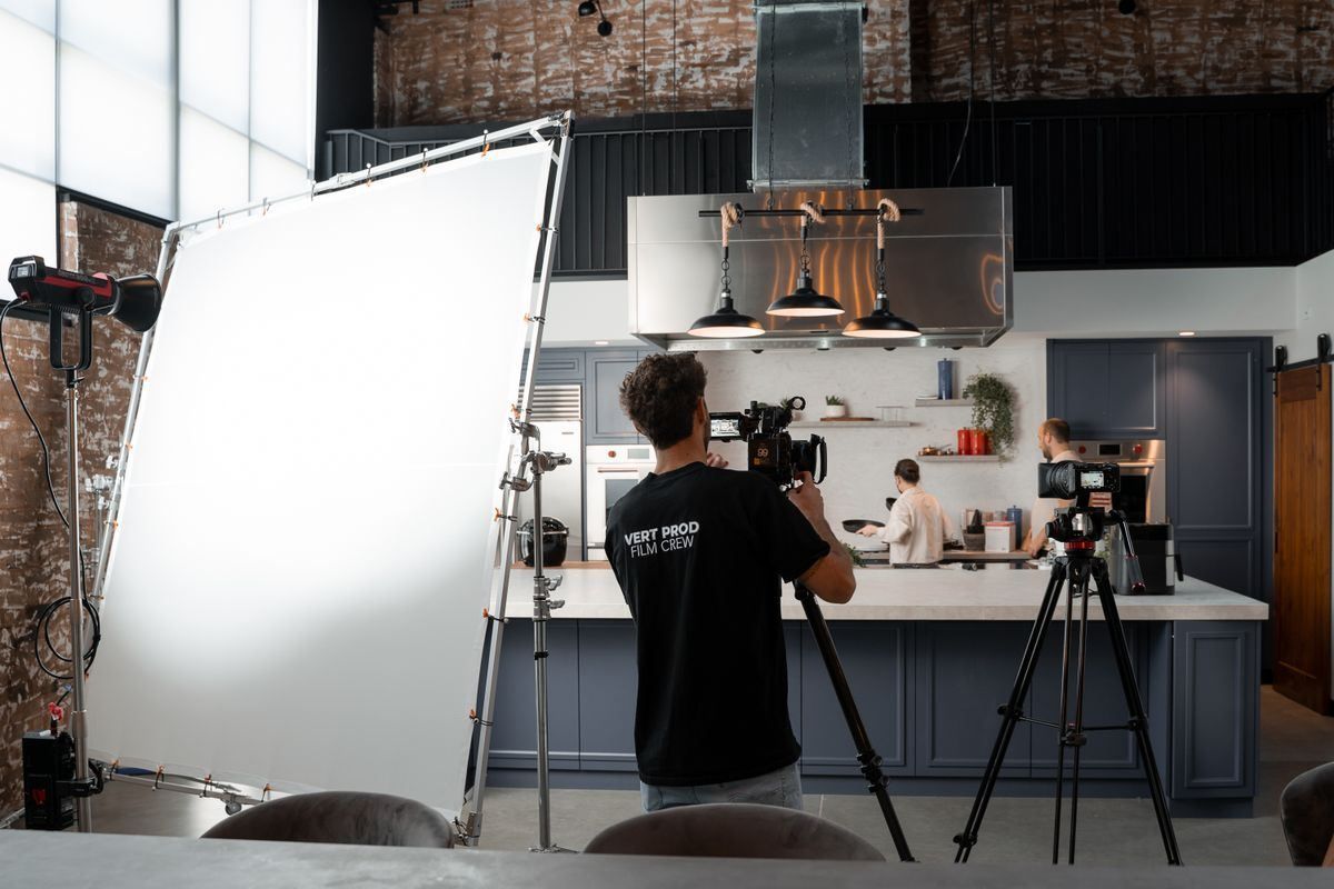 Film crew shooting in a modern kitchen set with lights, cameras, and a white backdrop