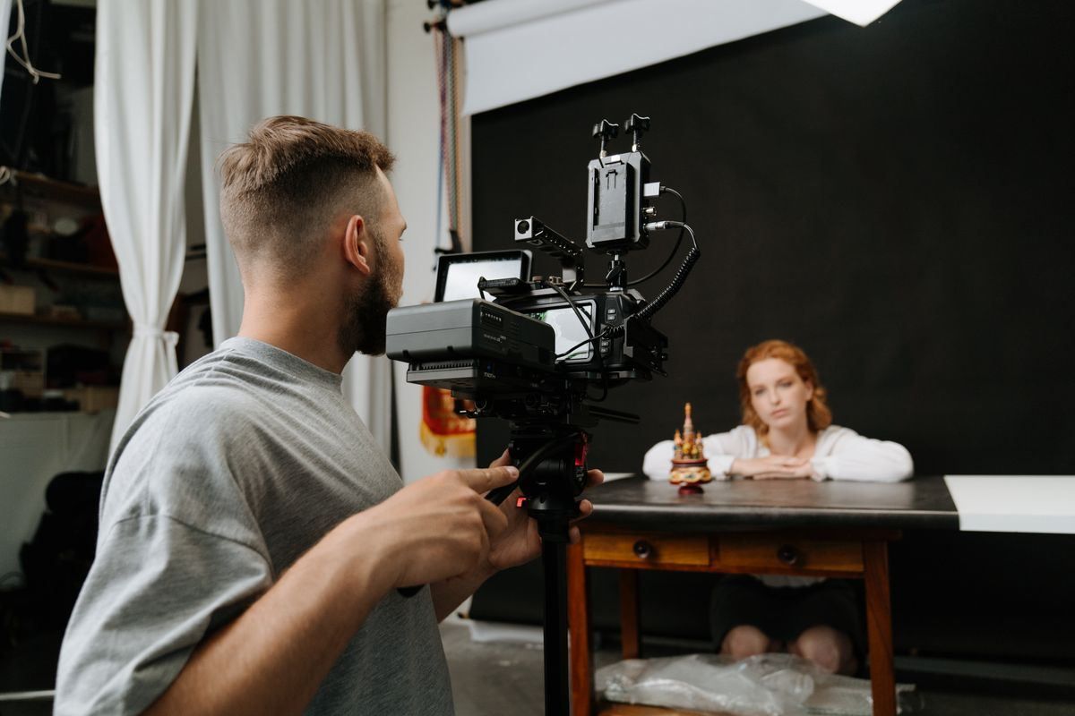 Photographer filming a seated subject in a studio with a black backdrop and soft lighting