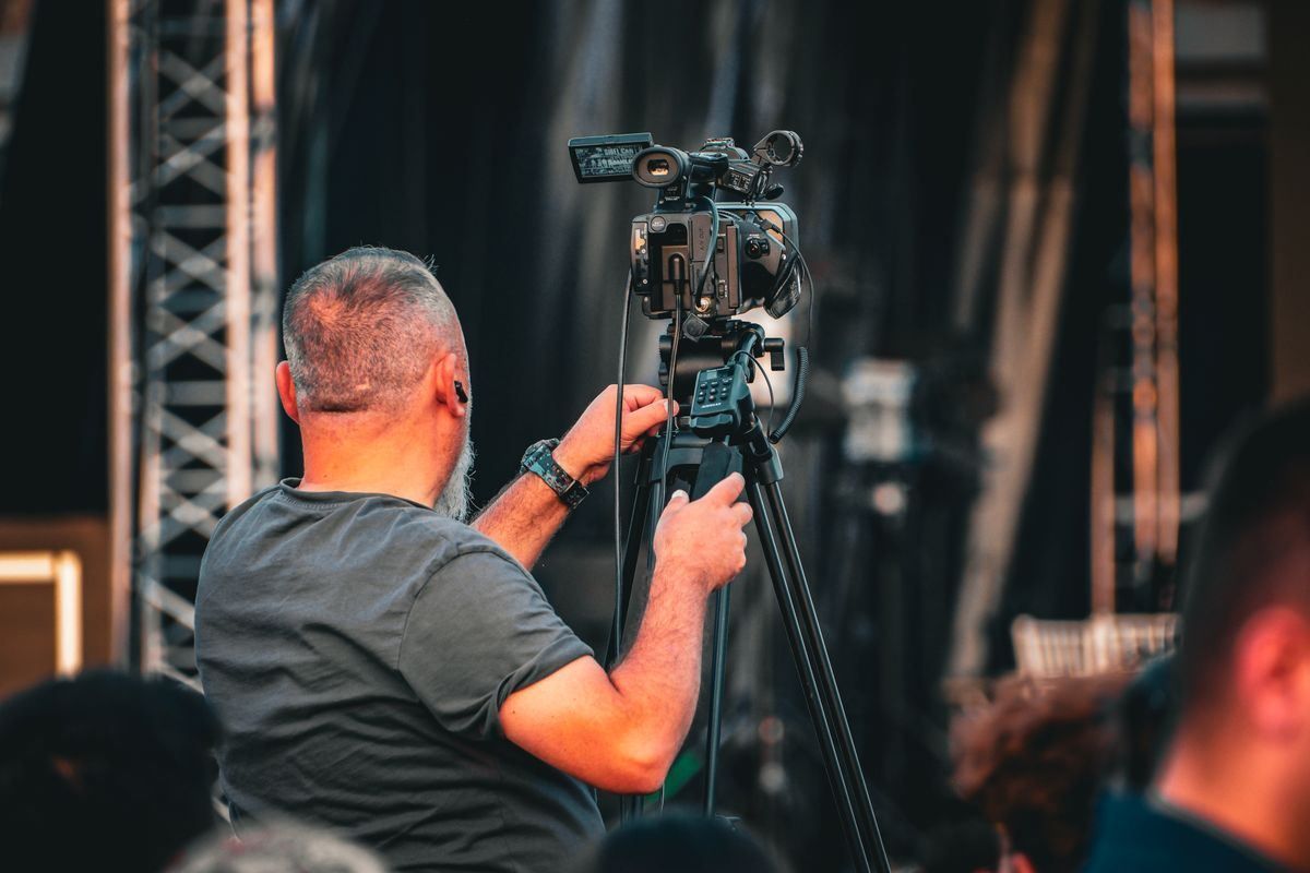 Cameraman adjusting a video camera on a tripod at a live stage event