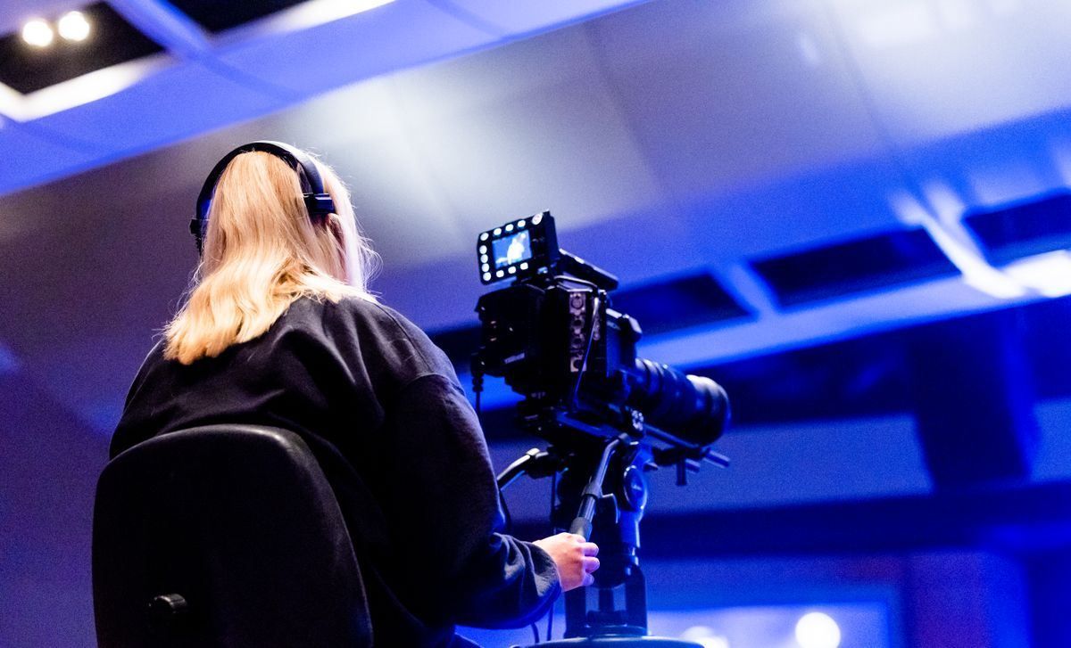 Camera operator filming in a blue-lit studio wearing headphones