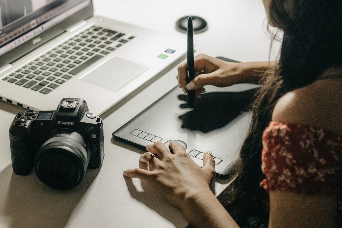 Person working on a graphics tablet beside a camera and laptop on a desk
