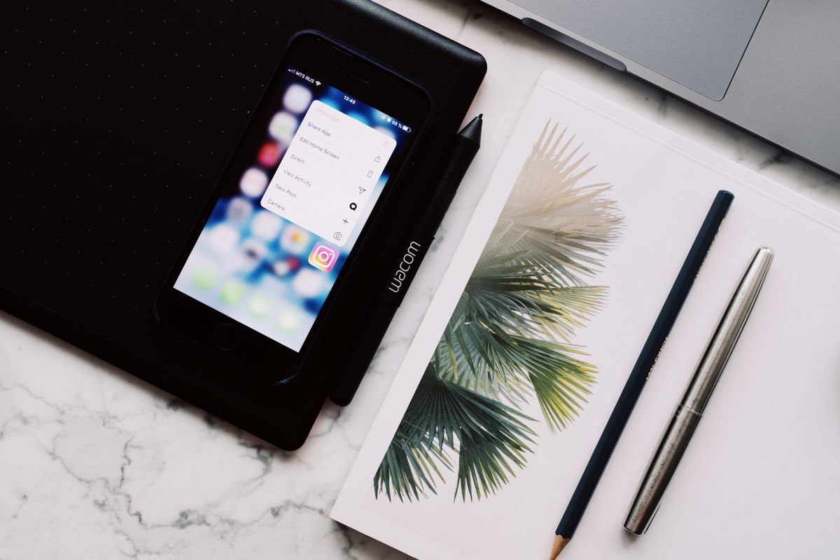 Desk with a smartphone, palm-leaf notebook, pencil, and pen on a marble surface.