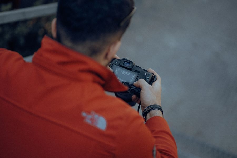 Person in a red jacket holding a camera, seen from behind outdoors.