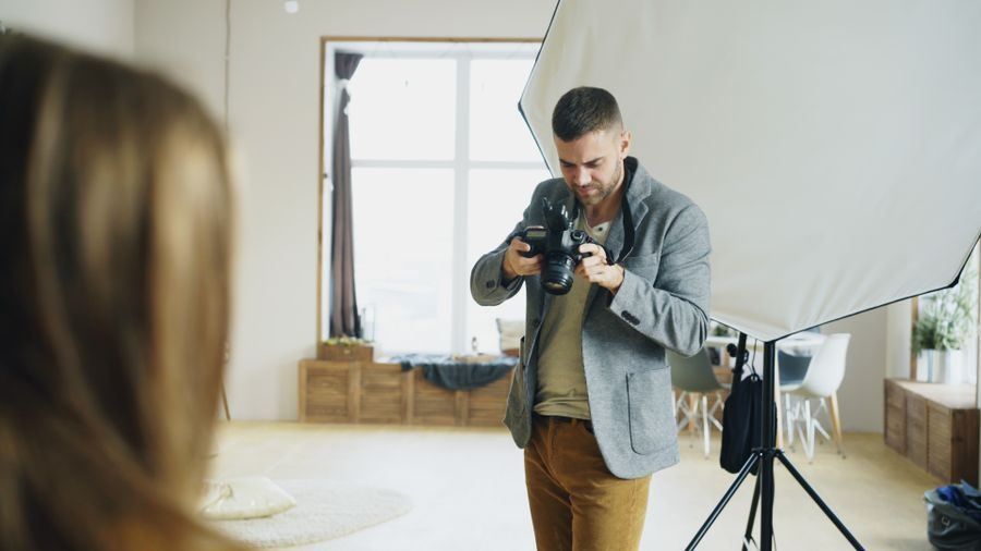 Photographer adjusting camera in a bright studio with a light reflector and large window
