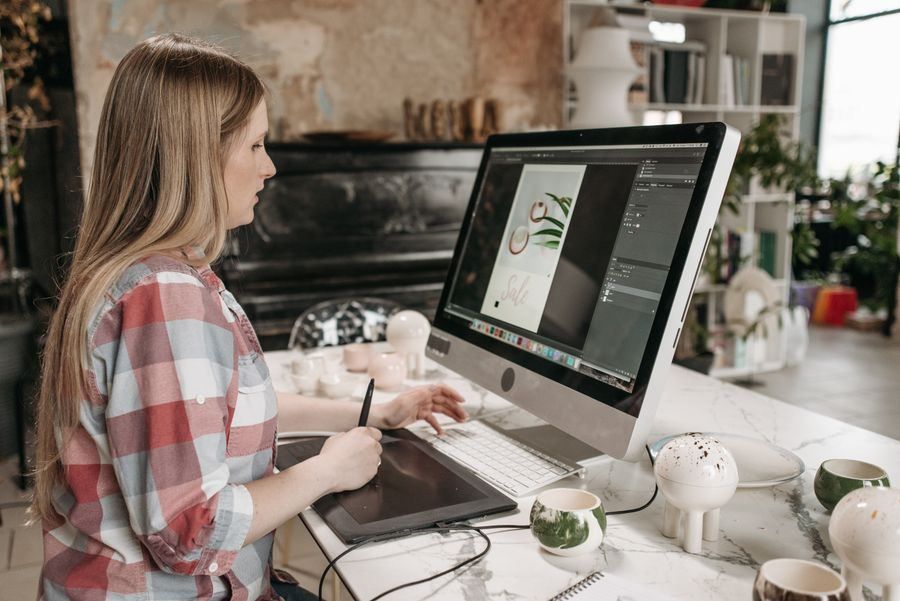 Woman sketching on a graphics tablet at a desktop computer in a bright home office
