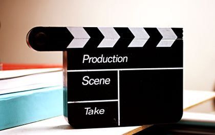 Black film clapperboard with white stripes and labels for production, scene, and take on a white background