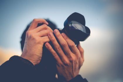 Hands holding a camera up to their face against a blurry sky background.