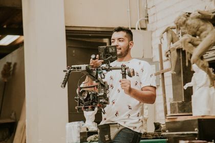 Man operating a camera rig in a studio, with a blurred sculpture in the background
