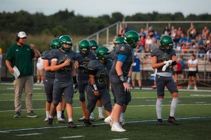High school football players in green helmets huddle on the field during a game at sunset