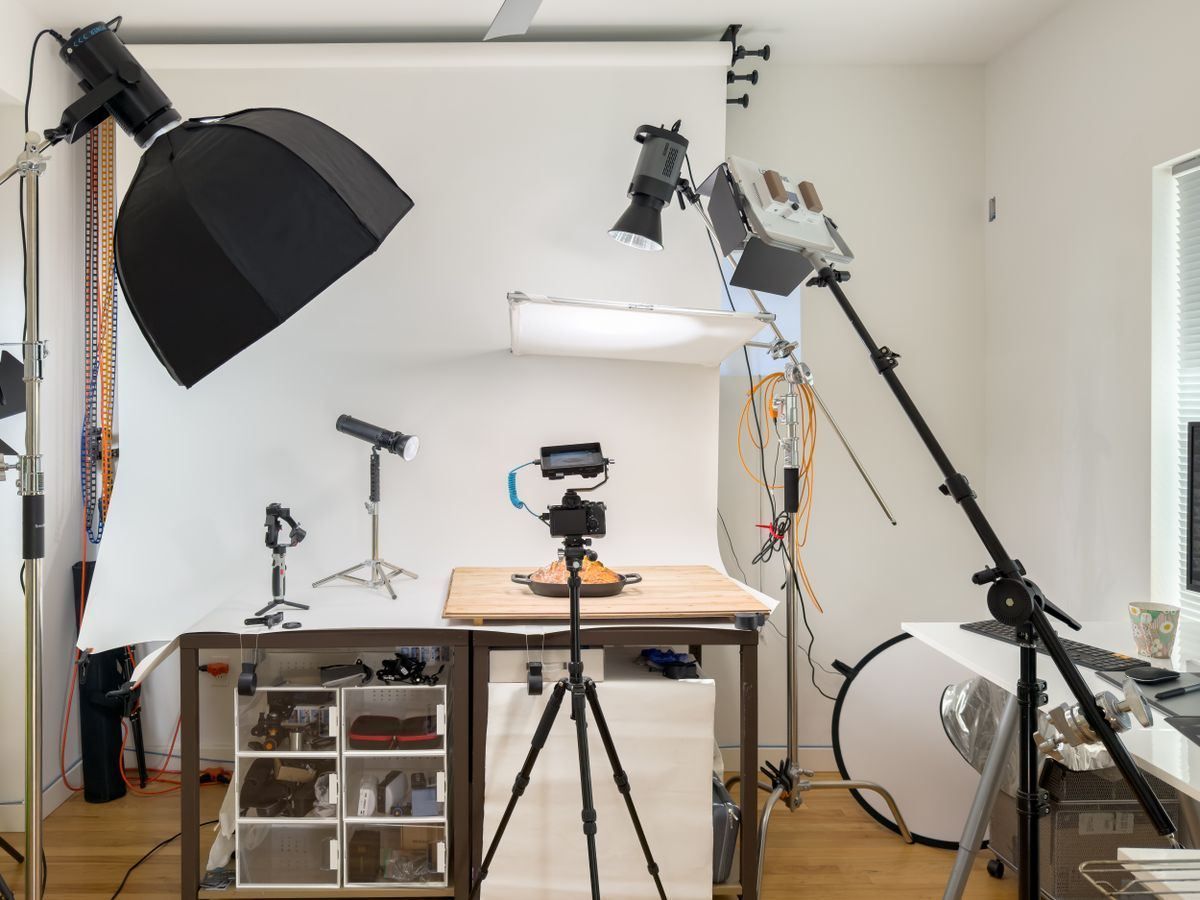 Studio with camera on tripod, lighting gear, white backdrop, and worktable for photo or video setup