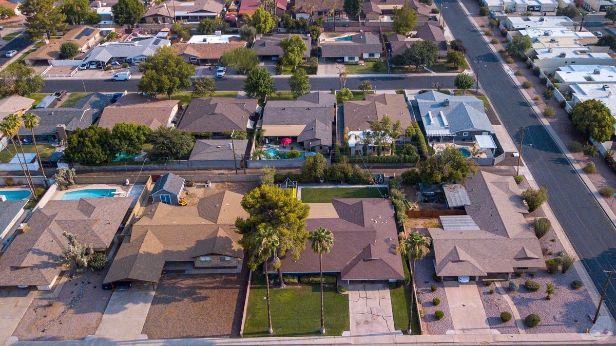 Aerial view of a suburban neighborhood with single-story homes, driveways, and a street lined with trees.