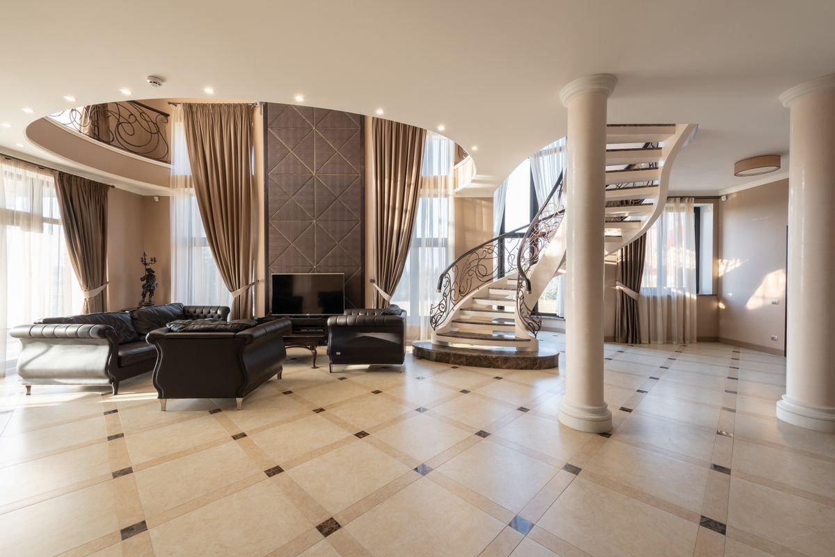 Luxurious living room with curved staircase, white columns, black sofas, and large windows