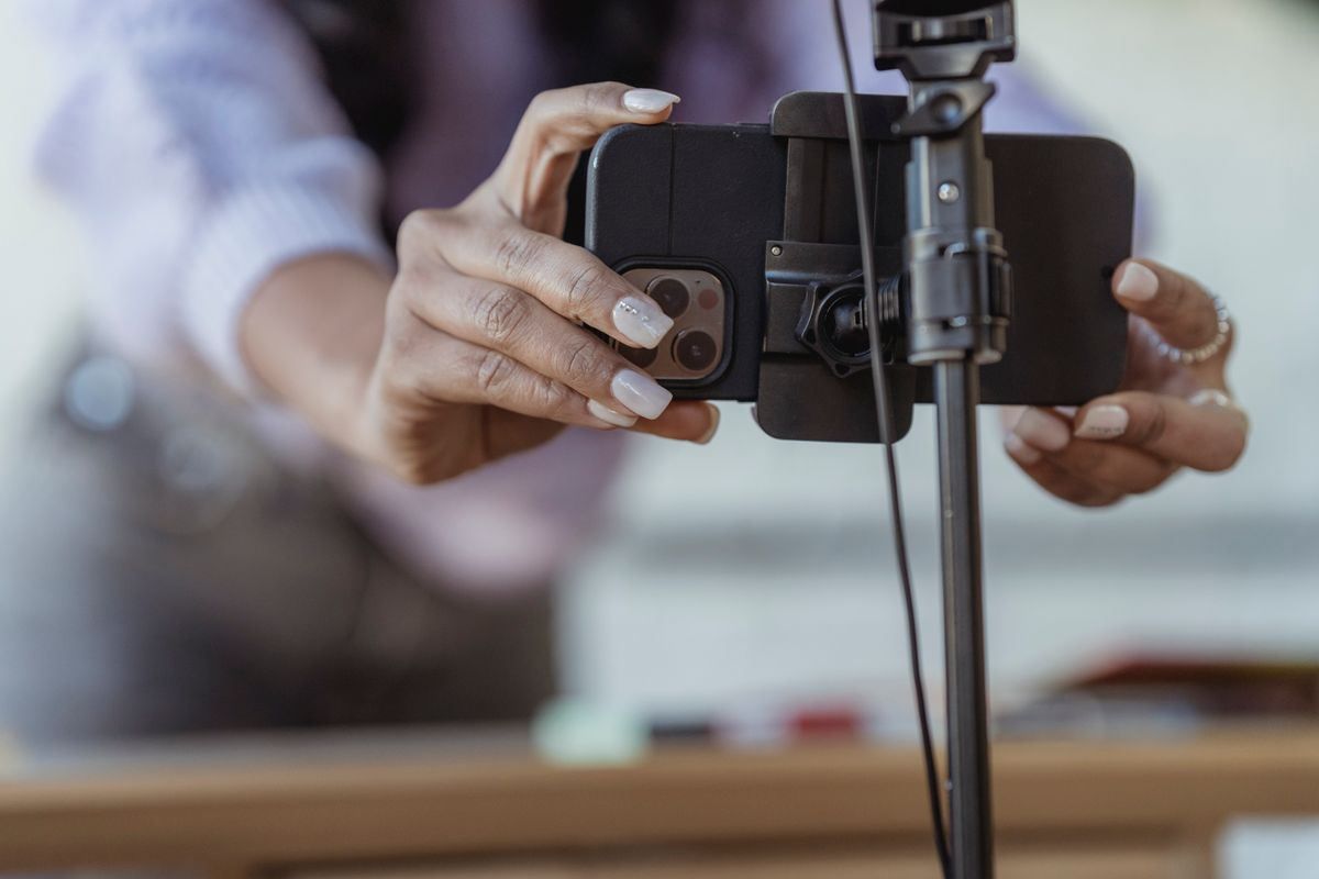Hands adjusting a smartphone on a tripod, with a blurred person in the background.