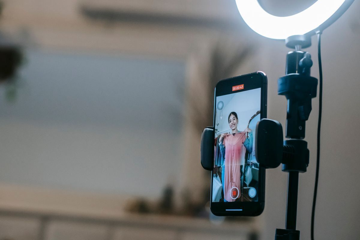 Smartphone on a tripod filming a woman in a pink dress beside a bright ring light