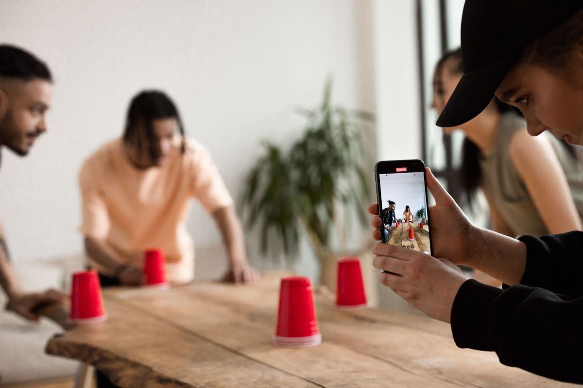 People playing a cup-and-ball game at a wooden table, filmed on a smartphone