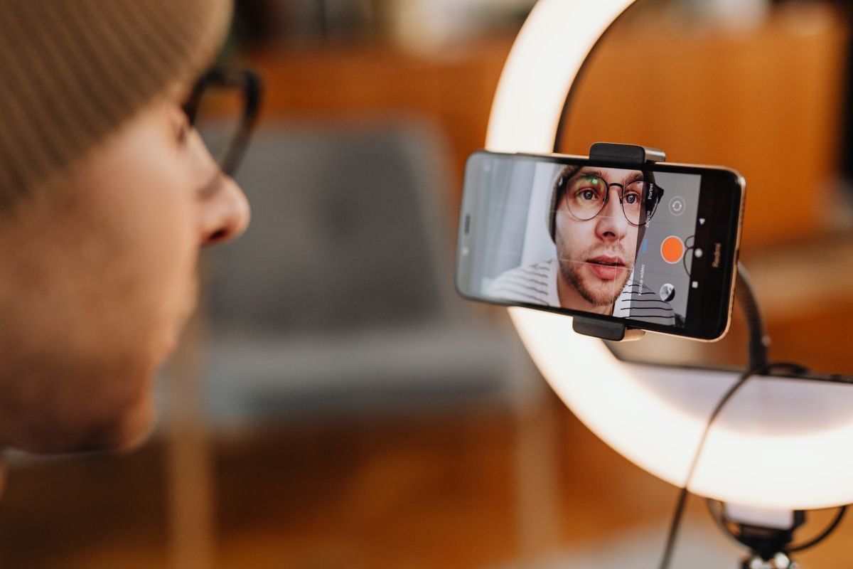 Smartphone on a ring light tripod showing a person’s face for a video call or recording