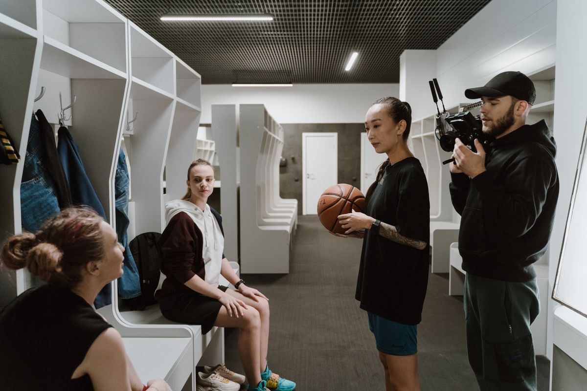 Woman being interviewed in a locker room while a cameraman films her.