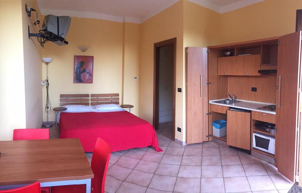 Piccolo monolocale giallo con letto, cucina e tavolo rossi.