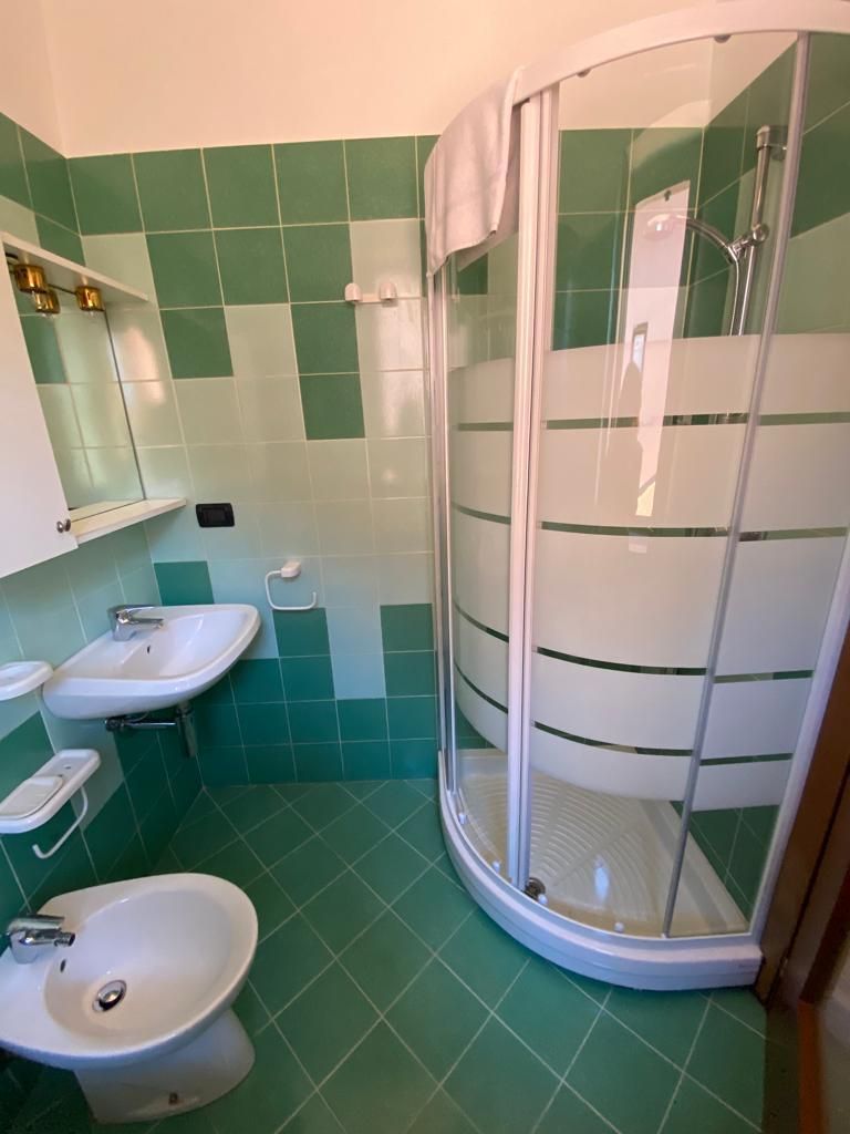 Bagno piastrellato di verde con doccia, lavandino, bidet e mobiletto.